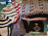 Photo showing six scarves folded showcasing different knit styles and colors, and four hats including striped and cable knit styles, also a black embellished hat.