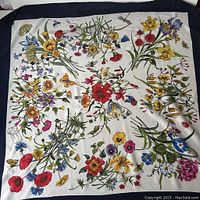 Full view of square silk scarf with multicolored floral print and navy border laid flat.