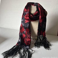 Full view of the silk scarf draped on a mannequin showing the red roses design and black tassels.