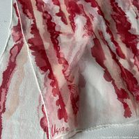 Close-up of Vera Sheer scarf fabric showing red abstract pattern and 'Una' signature