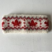 Clear full view of the knit ski head band showing red maple leaf pattern on white wool background.