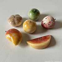 Photo of the set of 8 carved alabaster fruits from above on a plain surface, showing a variety of colors and types.