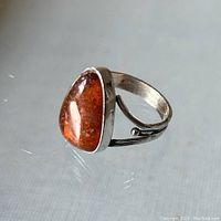 Angle showing pear shaped amber gemstone with sterling silver band and open side setting, amber is translucent with natural inclusions.