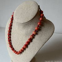 Coral necklace displayed on a mannequin bust against a white background, showing gradation of red and pink coral beads.