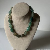 Front view of green agate oval bead necklace displayed on a beige necklace stand, showing the graduated green and beige tinted beads.