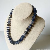 Front view of grey-blue polished faceted gemstone necklace on display bust, showing irregularly cut stones with blue and grey color tones.