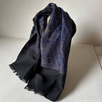 Overall view of the folded dark woven scarf with blue and black geometric pattern, displayed standing up to show texture and pattern detail.