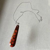 Full view of the wooden pendant and silver chain laid flat on a light fabric surface showing the pendant's design and chain clasp.