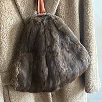 Front side of the mink muff showing the brown mink fur texture and leather strap handle attached with lucite hardware.