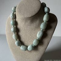 Front view of the necklace displayed on beige bust, showing large mint green Amazonite beads alternating with smaller spacer beads.