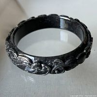 Close up of the carved dark omphacite jade bangle showing detailed floral scroll work.