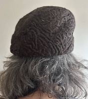 Persian lamb hat shown fitted on mannequin head, displaying the textured curly fur surface and dusty brown color.