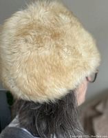 Side and back view of the beige shearling hat on a model, showing fuzzy texture and rounded fit.
