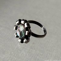 Side angled view of vintage sterling silver adjustable ring with abalone center set in flower-shaped design, showing silver band and curled petals.