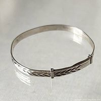 Front angle view of sterling silver child's adjustable bangle showing etched arrow pattern and adjustment sliders.