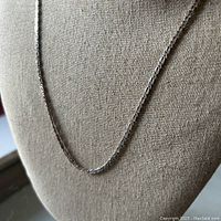 Front view of a silver flat anchor chain necklace displayed on a beige fabric jewelry stand, showcasing the chain's style and length.