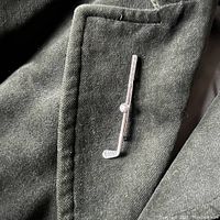 Close-up photo of the golf club pin worn on fabric showing smooth polished shaft, golf ball detail, and textured club head.