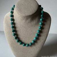 Front view of turquoise bead necklace displayed on beige jewelry stand to show bead size and color