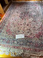 Full view of the floral patterned area rug showing overall pattern, color, and condition with visible stains and dirt.