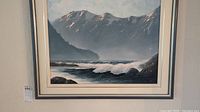 Framed oil on canvas painting showing coastal scene with mountains and ocean waves, signed in lower right corner.