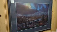 Framed artwork showing a mountain landscape with northern lights and a river under a night sky.