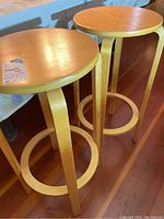 Pair of 2 wooden barstools with round tops and circular footrest, natural light wood finish.