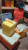 Photo showing multiple camping gear items arranged on floor, including two coolers, yellow water container, camping chair, and backpacks.