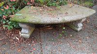 Full view of the concrete garden bench showing the top surface covered with leaves and moss.