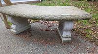 Concrete garden bench showing shape, decorative edge, and pedestal legs.