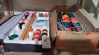 Two croquet sets shown side by side on a shelf, one in white foam packaging and the other in a cardboard box