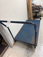 Side view of the blue metal platform with tubular handle and visible surface wear and rust.