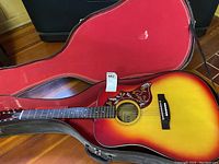 Full view of sunburst guitar seated inside open hard case with red interior