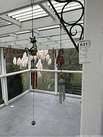 Wide shot showing hanging stained glass cat and owl ornaments with metal tubes and hanging bells, suspended from ceiling.