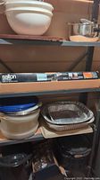Metal shelving shelf with white plastic mixing bowls stacked on top, containers, and aluminum trays below.