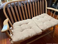 Full view of wooden loveseat with two beige tufted seat cushions on wooden frame with armrests.
