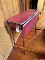 Side view of red drop leaf table showing metal legs and trim along the edges.