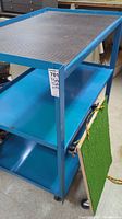 View of the full blue metal trolley showing three shelves and caster wheels.