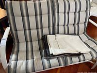 Full view of the rocking patio loveseat with metal frame and striped seat and back cushions. Four fabric covers folded on the seat.