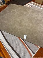 Top view of a solid beige area rug with plush texture laid over a patterned rug.