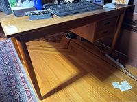 Front view of teak desk on hardwood floor showing two drawers and tapered legs