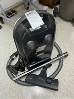 Full view of Miele vacuum canister with hose wrapped around and main floor head attached, showing overall condition and accessories included.