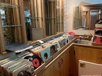 Long countertop with multiple open cardboard boxes holding vertically stored 45 rpm records in sleeves, mirror background