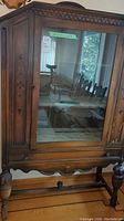 Front view of vintage wooden cabinet with glass door, decorative carvings on the wood panels and turned wooden legs.