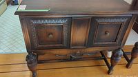 Front view of vintage dark wood sideboard showing ornate carvings on drawer fronts and turned leg detail