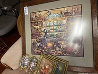Photo showing the largest framed print of a vintage pharmacy interior with many bottles and paraphernalia, alongside two smaller framed portraits and small oval floral prints.