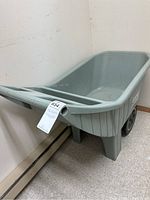 Gray plastic wheelbarrow positioned against corner walls, showing the full side and front profile.
