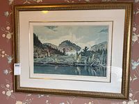Framed landscape print with ornate gold frame hanging on floral wallpaper.