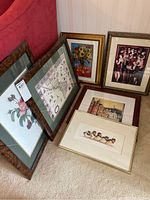 Six various framed prints arranged on the floor against a wall, showing different subjects: roses, map, sunflowers, village, party, and birds.