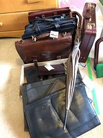 For sale: multiple leather briefcases and portfolios in various colors and conditions including a brown Bugatti briefcase. Also visible is a beige umbrella leaning against the bags.