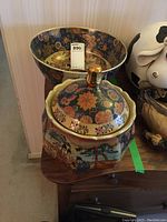 Large Satsuma lidded bowl with figurative scenes and gold floral pattern next to a deeper large Satsuma bowl with detailed interior decor